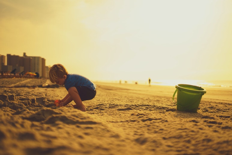Enfant sur la plage avec son seau, sa pelle entrain de faire des châteaux de sable