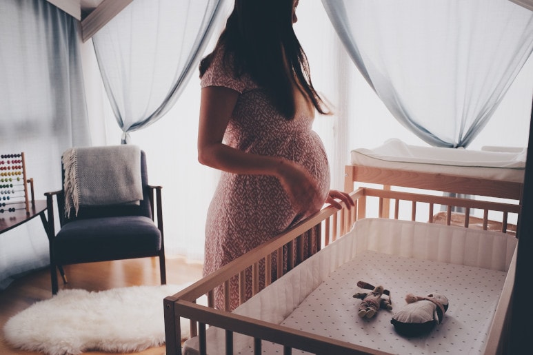femme enceinte debout devant un berceau vide
