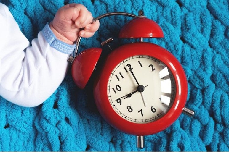 Réveil rouge dans la main de bébé sur une couverture bleue