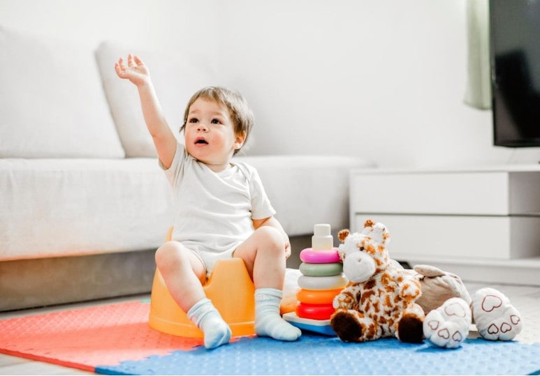 Petit garcon sur son pot levant le bras avec ses jouets dans le salon à la maison