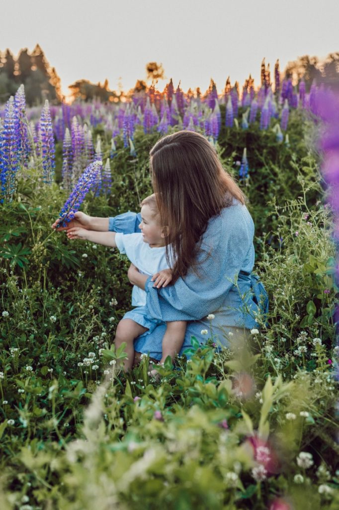 Une maman cueille des fleurs avec son enfant dans un champs vert et violet
