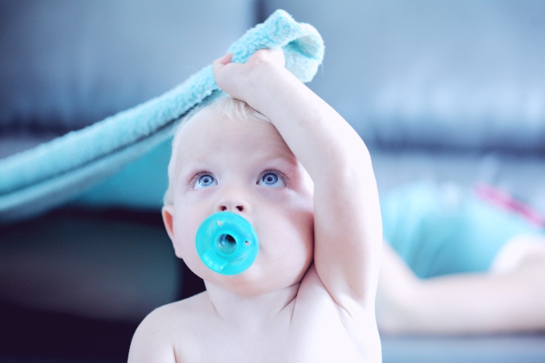enfant avec une tétine bleue tirant une couverture bleue