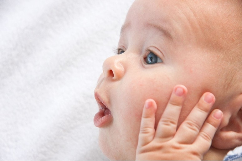 bebe avec la main sur la joue sur une couverture blanche