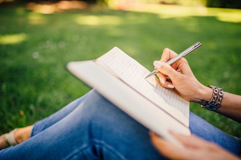 Ecriture dans un journal intime assis dans l'herbe au calme